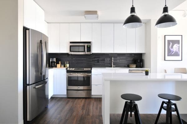 A modern kitchen with white cabinets, wooden floor, and a large fridge-freezer